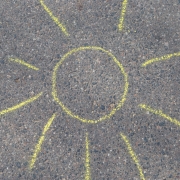 dessin de soleil à la craie jaune sur béton gris