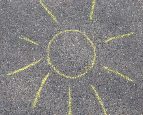 dessin de soleil à la craie jaune sur béton gris